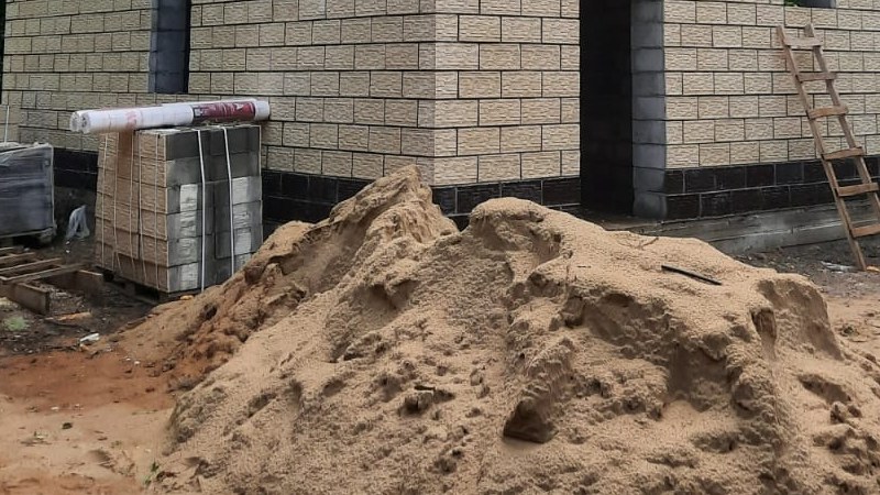 Цоколь дома из теплоблока с тёмной гидроизоляционной полосой у основания стены на строительной площадке